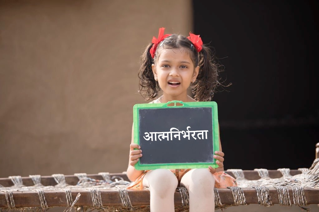 small girl holding black slate with Atmanirbharta written on it