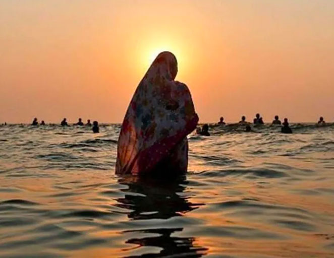 silhouette of a lady doing chhath puja at sunrise 