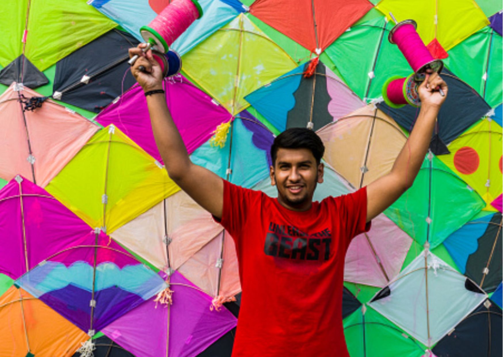 a man standing in front of a wall of kites during uttrayan, festival of kites